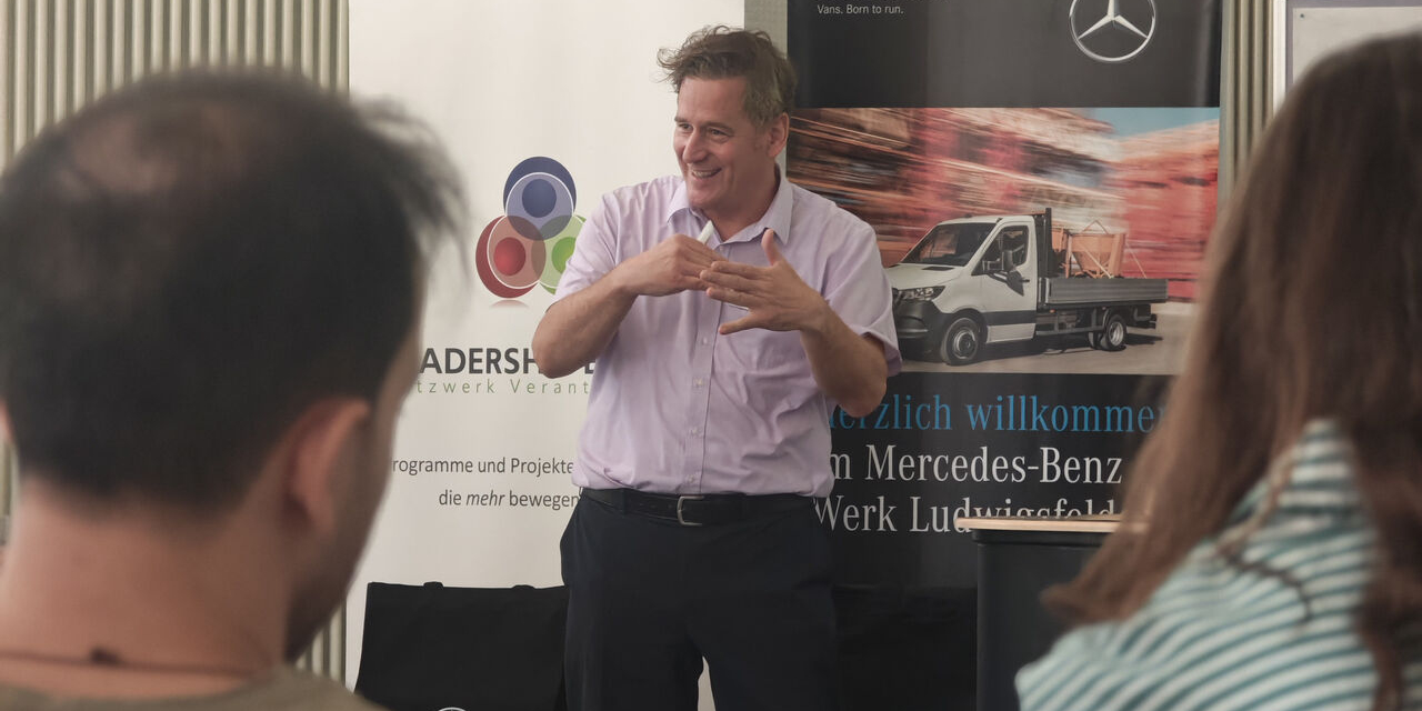 Ein Referent spricht mit den Teilnehmenden vor einem Mercedes-Benz-Banner.